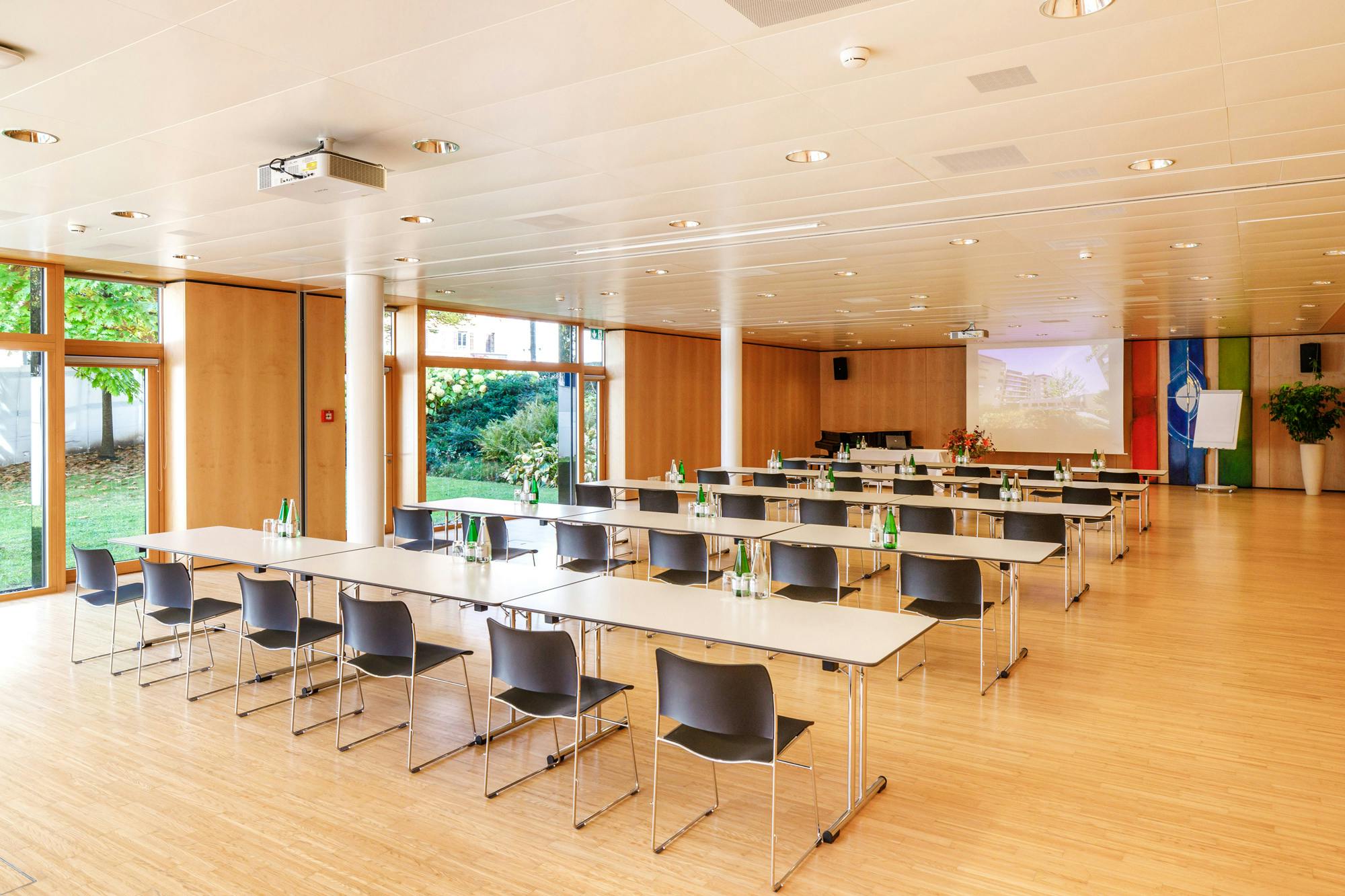 Leerer Konferenzraum mit Tischen in U-Form, Stühlen und Präsentationsbildschirm.