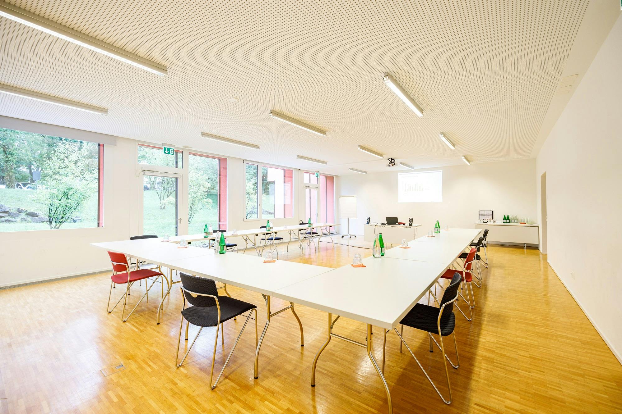 "Heller Seminarraum mit Tischen, Stühlen und Präsentationsbildschirm"