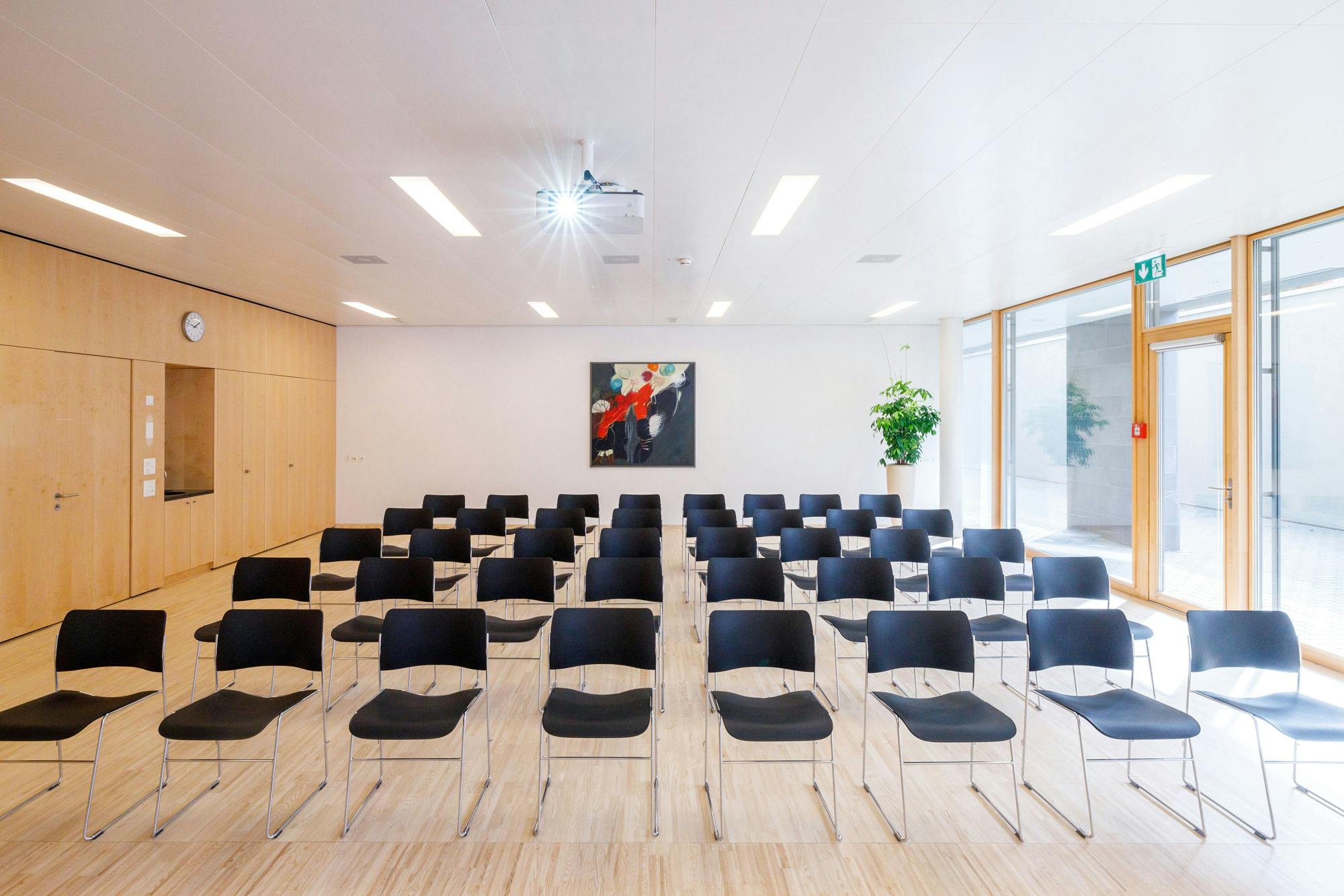 Konferenzraum mit Reihen von schwarzen Stühlen und einem abstrakten Gemälde an der Wand.
