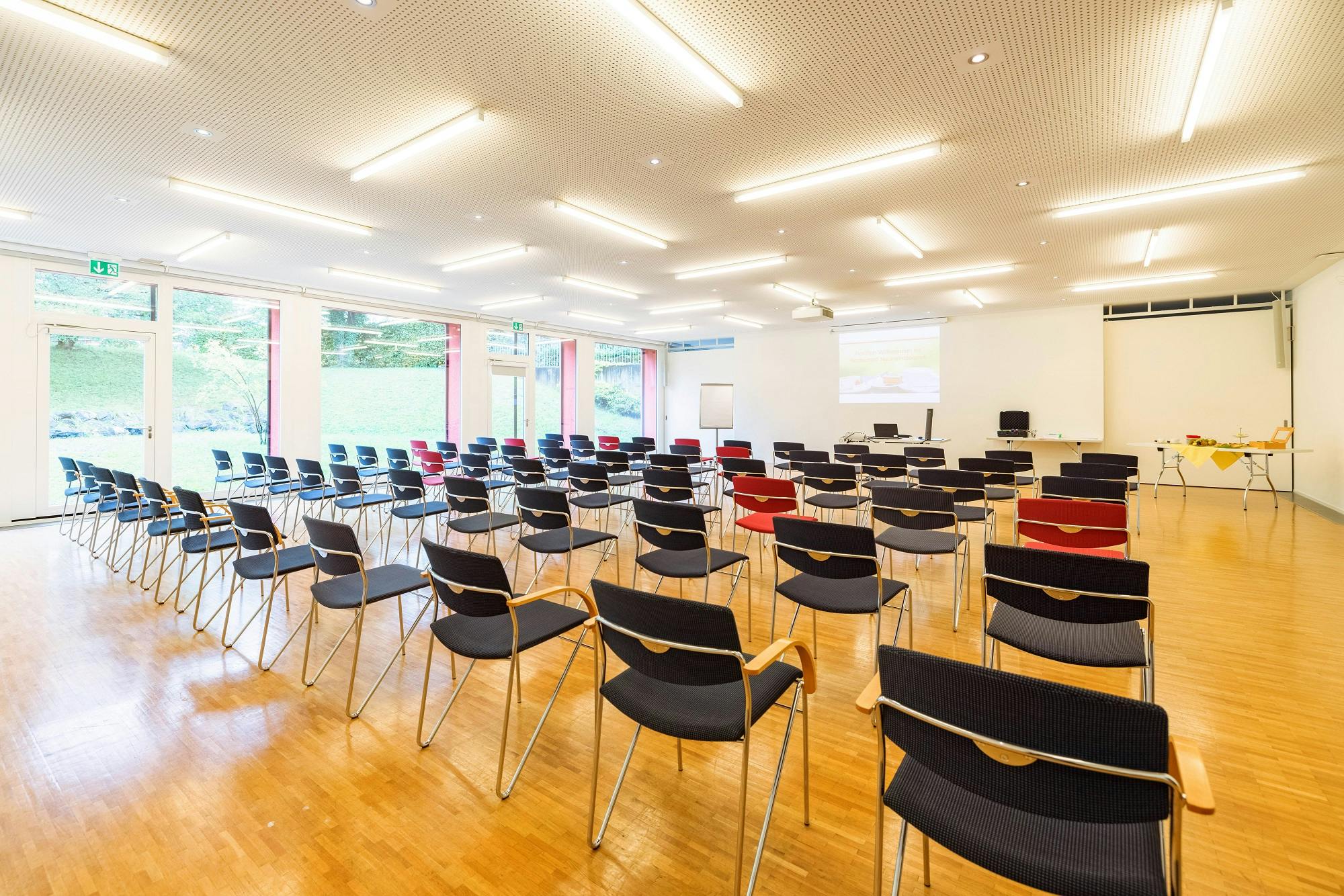 Leerer Konferenzraum mit Reihen von Stühlen und einem Projektorbildschirm.